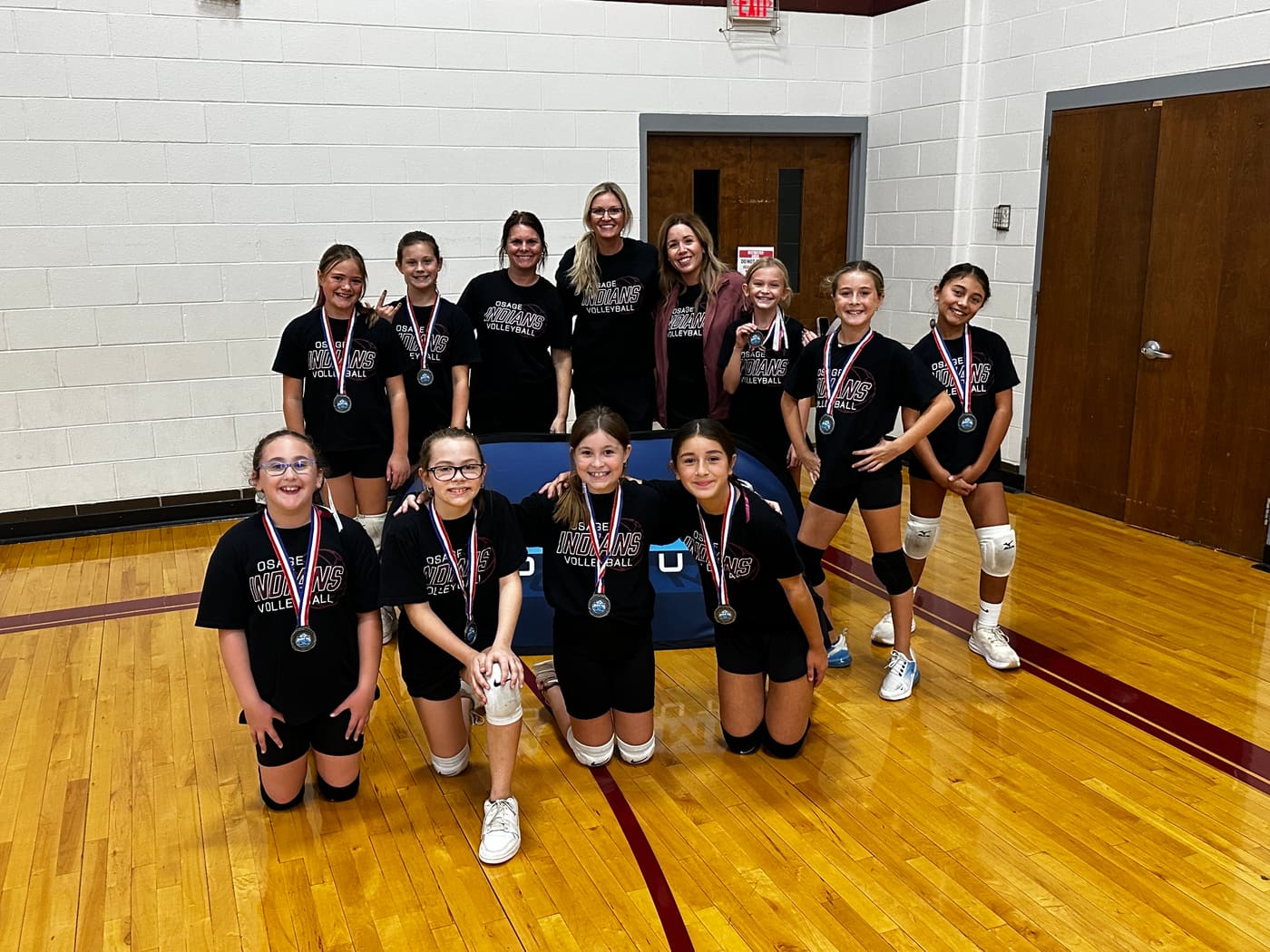 Osage Indians players in black shirts kneel and stand with their coaches, medals around their necks.