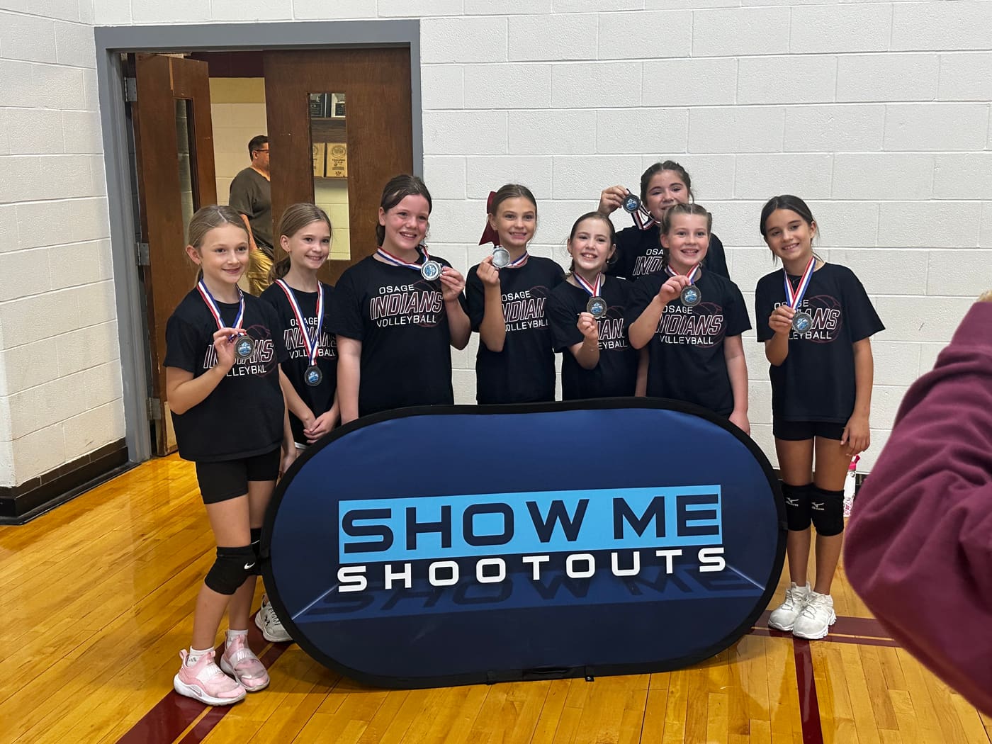 Younger Osage Indians players hold up their medals and grin for the camera.