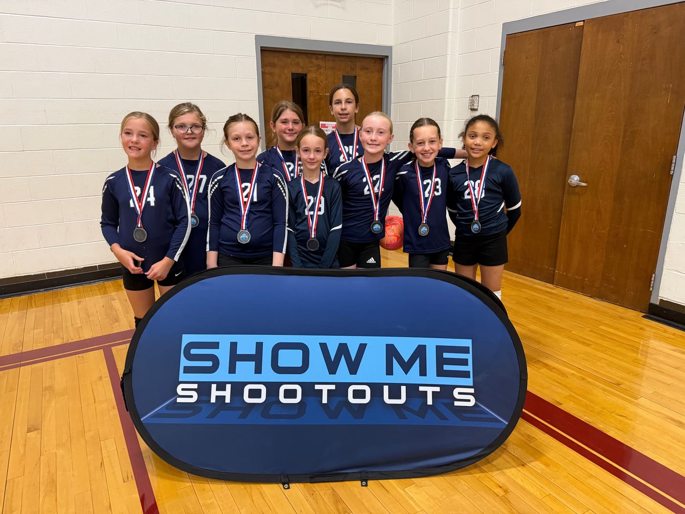 A team in navy numbered jerseys stands shoulder to shoulder wearing medals.