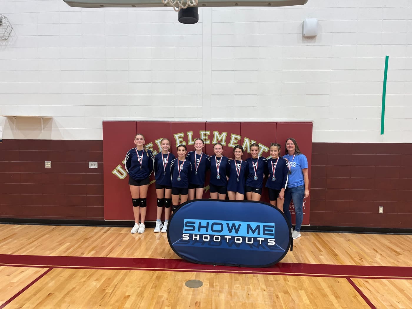 A team in navy long-sleeve jerseys lines up with their coach, each wearing a medal.